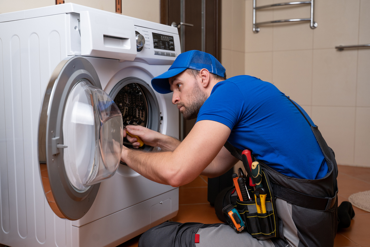 Working man plumber repairs a washing machine in home.