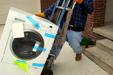 White washing machine on hand truck being moved by man in blue plaid and jeans
