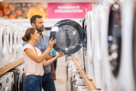 Young couple seen in a home appliances store in front of a laundry machine.