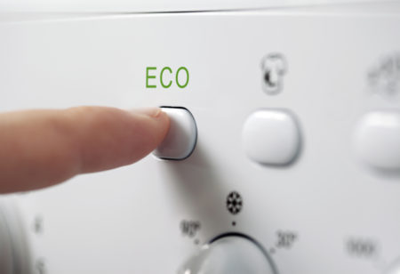 Finger pressing ECO button on washing machine.