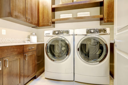 White and brown laundry room features modern appliances placed under shelves and cabinets. Northwest, USA.