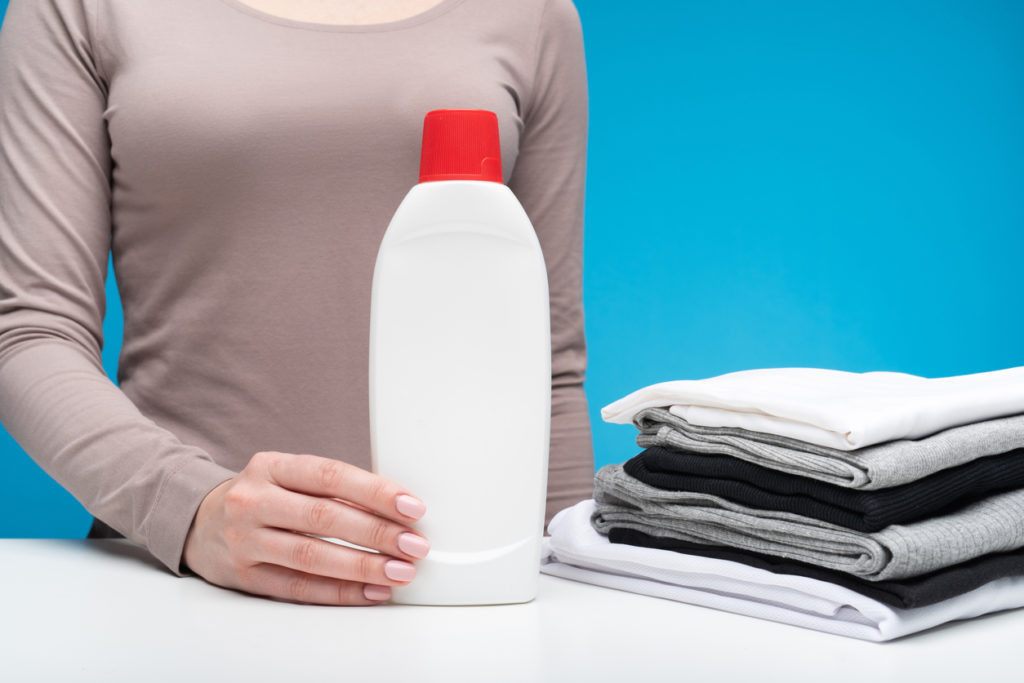 A woman standing with a bottle of detergent next to her.